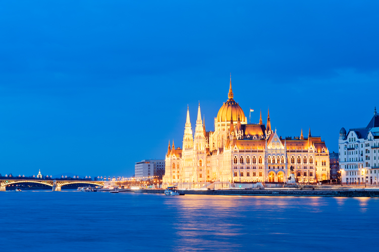 Illuminated Parliament building surrounded by blue dusk sky and Danube River, Budapest